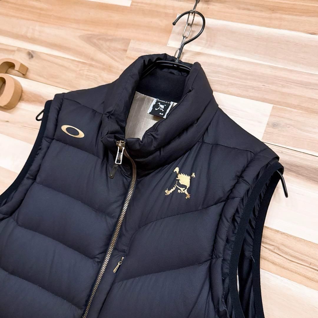 【オークリー】フェザー ブレンド スカル ロゴ ダウンベスト ゴルフ M 黒×金 オークリー】フェザー ブレンド スカル ロゴ ダウンベスト ゴルフ M 黒