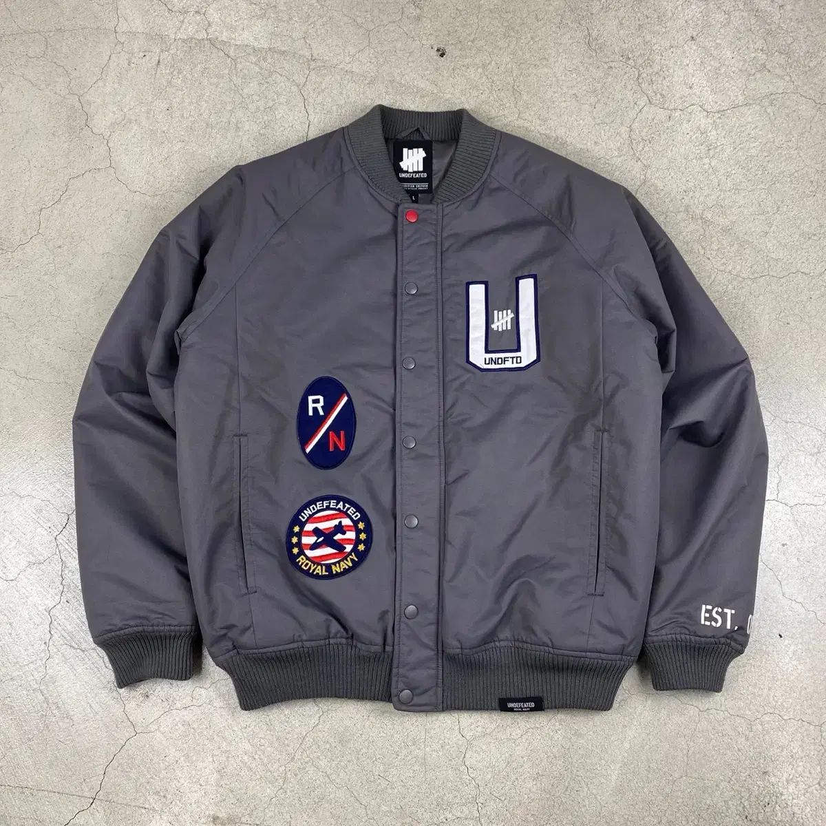 UNDEFEATED(アンディフィーテッド) ビッグロゴ グレー ボンバー ジャケット （ 100 ）