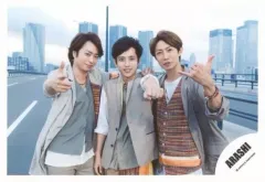 【中古】生写真(ジャニーズ) 嵐/集合(3人)/横型・上半身・衣装ベージュ茶グレー白・センター二宮・左手グー突き出し・櫻井右手指差し・相葉左手指2本立て・背景野外・道路・ビル/「Power of the Paradise」PV＆ジャケ写撮影/公式生写真