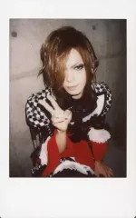 【中古】生写真(男性) D/HIDE-ZOU/膝上・衣装黒・赤・ブロックチェック柄・椅子座り・右手ピース胸元・左手下・背景コンクリート壁/生チェキ